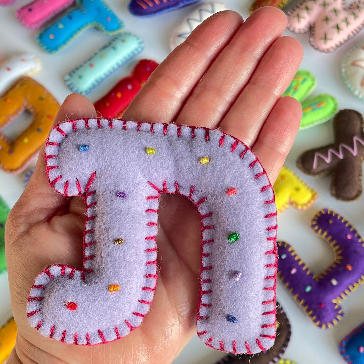Hand holding Hebrew felt letter toy with colorful letter toys in the background.
