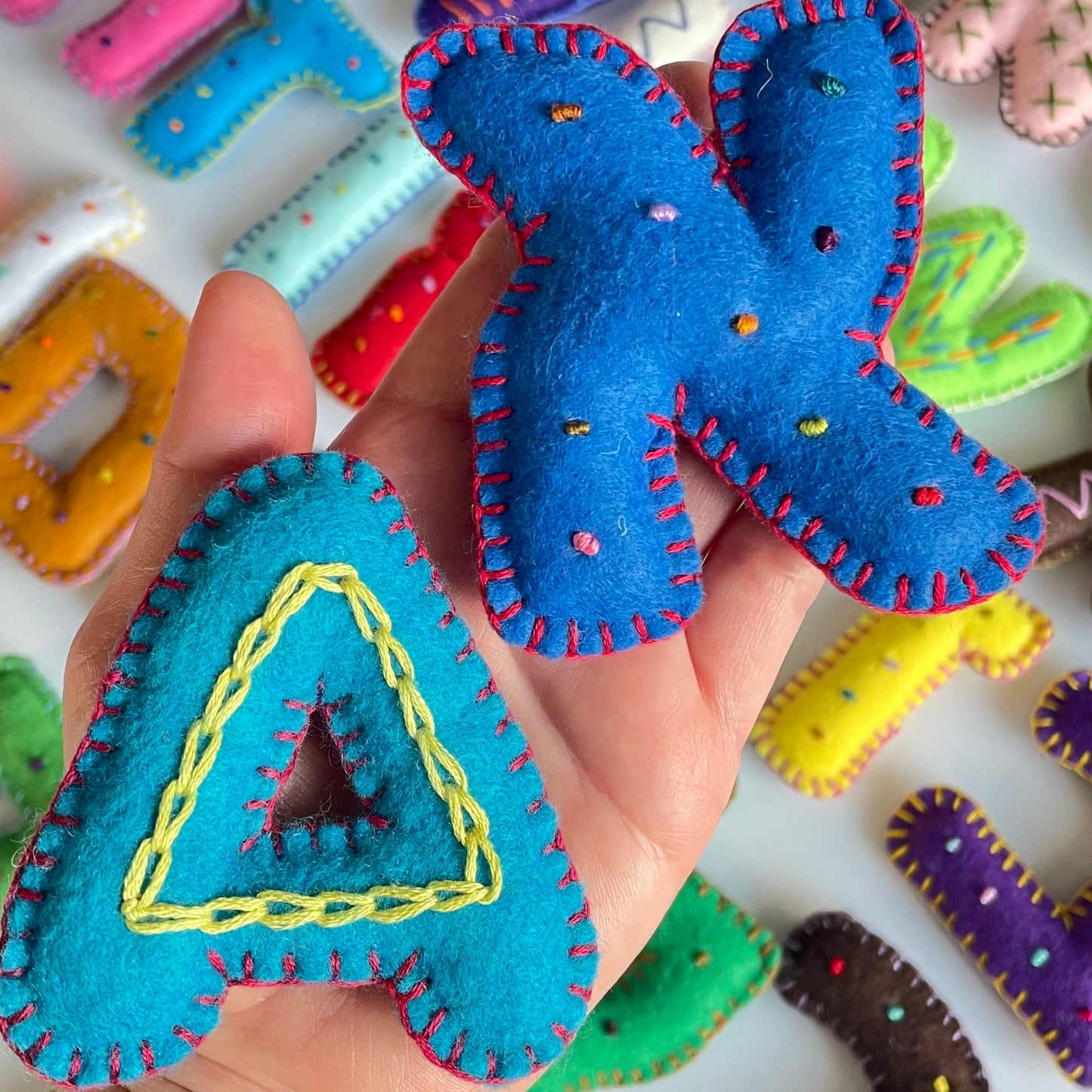 Colorful English Hebrew aleph and a shaped toys held by a hand with a background of more letter toys.
