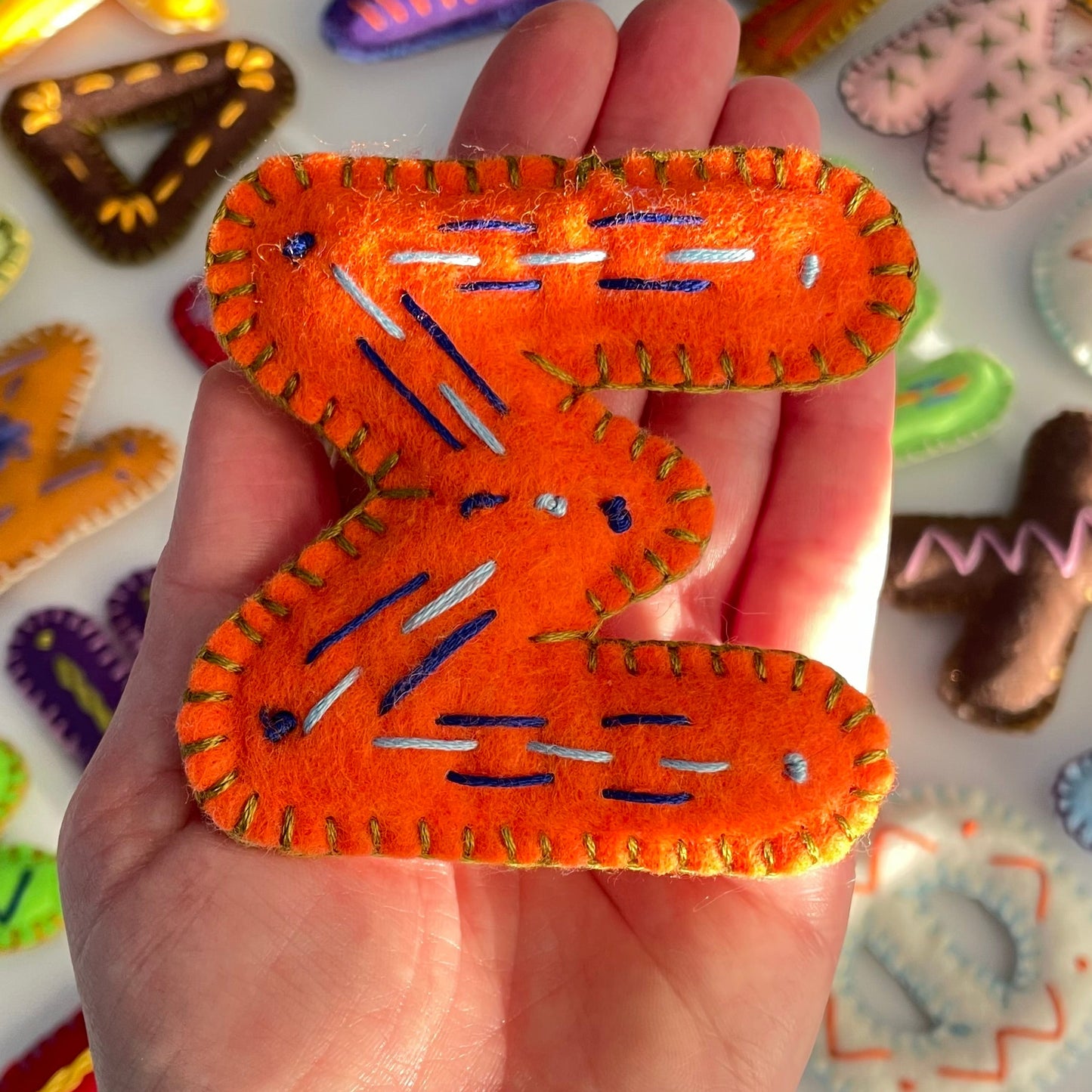 Hand holding a Greek Letter Sigma orang with colorful letters in the background