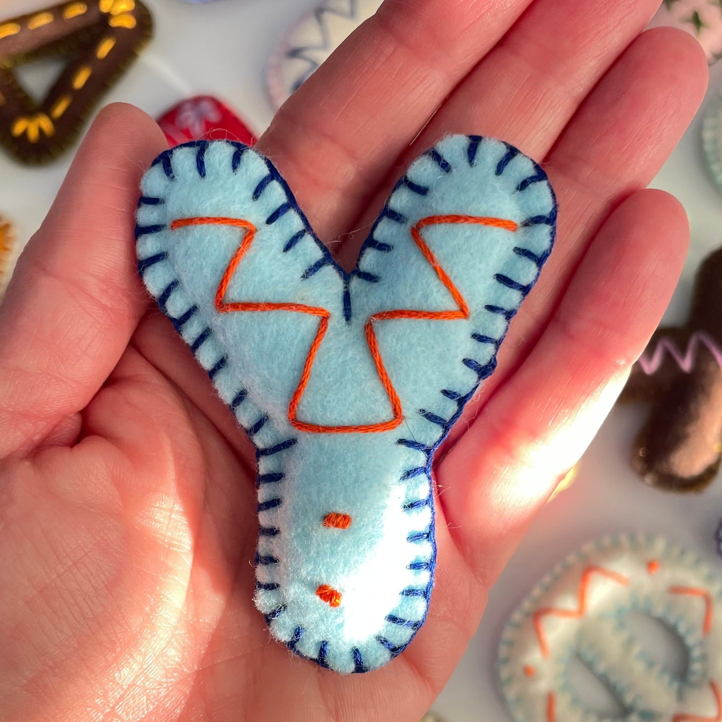 Hand holding a blue Y letter shaped felt ornament with orange accents against a colorful background of similar ornaments.