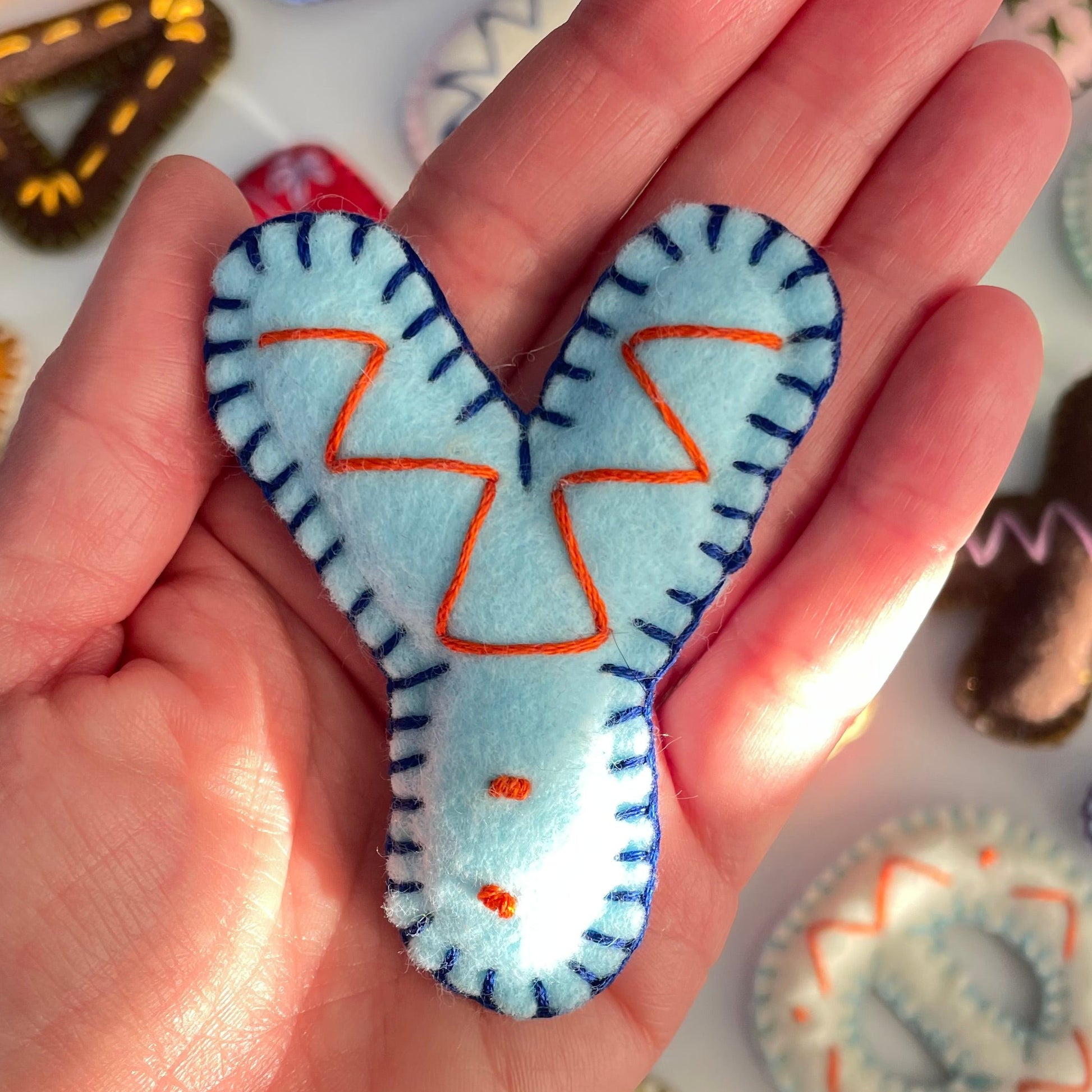 Hand holding a blue Y letter shaped felt ornament with orange accents against a colorful background of similar ornaments.