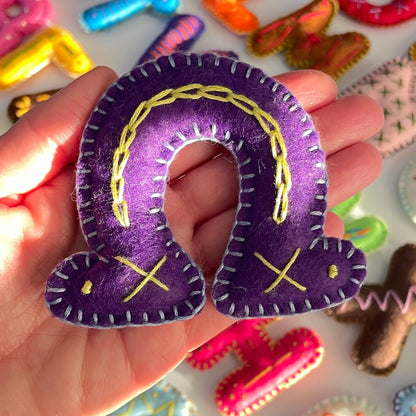 Hand holding handmade Greek  letter "Omega" with colorful letters in the background